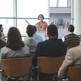 Businesswoman speaking animatedly to crowd of business people at business seminar in office