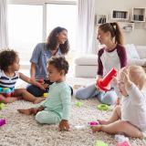 Two friends playing with toddler kids on sitting room floor