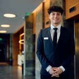 portrait-of-happy-concierge-in-hotel-lobby-looking-2024-12-13-20-30-13-utc