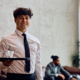 Portrait of happy waiter working in a hotel and looking at camera. Copy space.