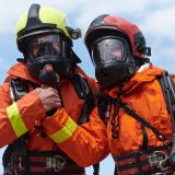 A unified team of firefighters, adorned in their uniforms, engages in a heartfelt celebration marked by triumphant salutes and cheers, embodying the joy and gratitude following the successful completion of a challenging firefighting mission.