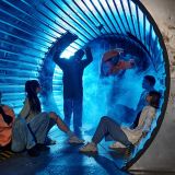 multiethnic friends sitting in tunnel near freaky people in gas masks,  quest room adventure