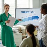 Young businesswoman with report pointing at screen with graphs and giving new information to her colleagues at training