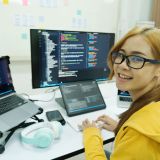 Young programmer or IT specialist satisfied with her work done. Happy young woman working on laptop while sitting at her working place in office.