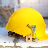 Construction yellow hardhat and key to house on window of housing made of blocks of porous concrete. Turnkey construction, future home, engineering, building. Work safety. Copy space