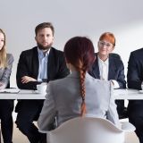 Woman during job interview and four businesspeople sitting by office table