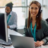 Happy customer service representative working at call center office and looking at camera.