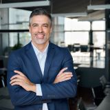 Happy middle aged business man ceo standing in office arms crossed. Smiling mature confident professional executive manager, proud lawyer, confident businessman leader wearing blue suit, portrait.