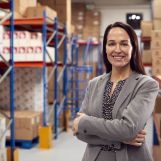 Portrait Of Female Team Leader Standing By Shelves In Warehouse