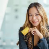 Asian businesswoman smiling and looking at camera in hand holding credit card for online shopping on mobile phone or laptop, online shopping.
