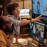Project manager pointing at big display and giving instructions to colorist during their work at office