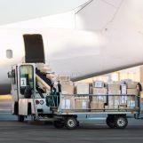 Close-up detail view of cargo cart trolley full with commercial parcels against turboprop cargo plane. Air mail shipping and logistics. Import export operations. Commercial charter flight service.