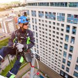Industrial mountaineering worker hangs over residential building while installing and repairing equipment. Rope access laborer hangs on wall of house. Concept of high-rise urban works. Copy space